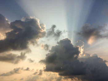 Low angle view of sunlight streaming through clouds