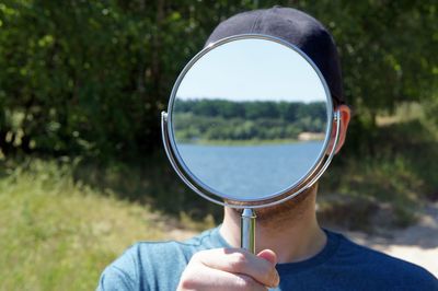 Headshot of man standing with mirror covering face