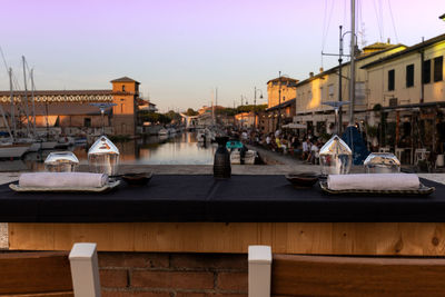 Sailboats moored on harbor by buildings against sky during sunset