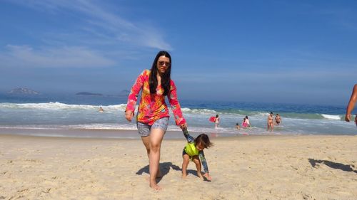 Mother holding hands of son while walking on sand against sea