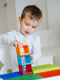 Cute toddler 3 years boy in grey pajamas playoing lego constructor in bright interior