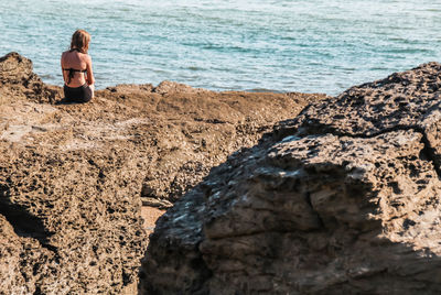 Rear view of young woman sitting on rock at beach