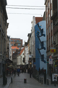 People walking on street amidst buildings in city against sky