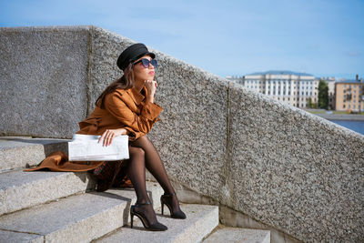 Young woman sits on the steps on the embankment with newspaper in hand