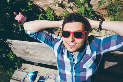 High angle view of smiling man with hands behind head wearing sunglasses during sunny day