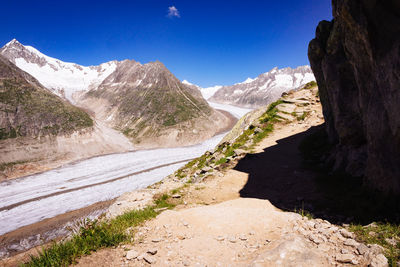 Scenic view of river by mountains against clear blue sky