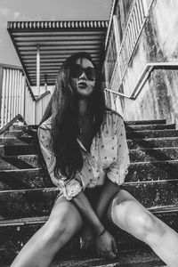 Low angle view of young woman wearing sunglasses sitting on steps