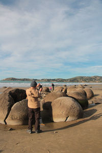 Rear view of man standing on rock against sky