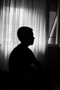 Side view of silhouette man sitting on window at home