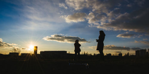 Silhouette mother and daughter standing on field against sky during sunset