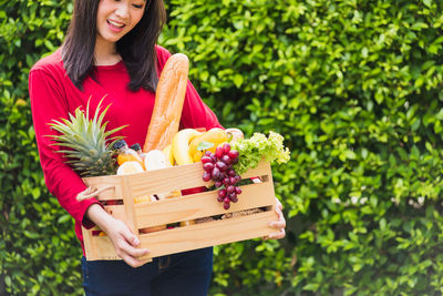 Midsection of woman holding fruits in container while standing outdoors