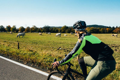 Rear view of man riding bicycle on field against clear sky
