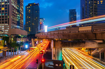 Light trails on street amidst illuminated buildings in city at night