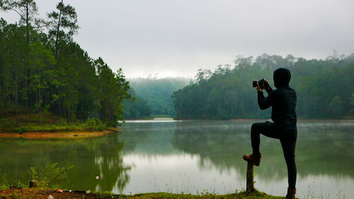 Man photographing by lake against trees
