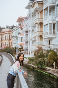 Portrait of young woman standing against buildings in city