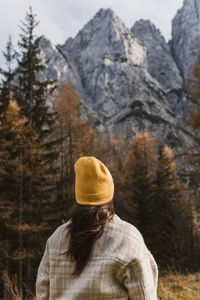Rear view of young woman standing under beautiful mountains in autumn