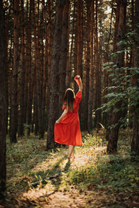 Alone woman in red dress dance on sun pine forest nature background