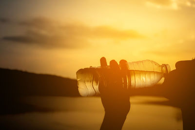 Close-up of silhouette woman drinking water from bottle against sky during sunset