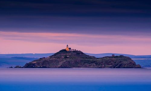 Lighthouse by sea against sky during sunset