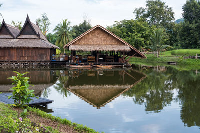 Traditional wooden thai house by canal with wood boat and skyline reflection on water.