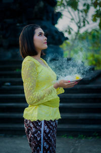 Young woman looking away while standing outdoors