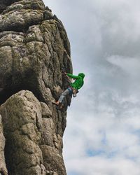 Low angle view of man climbing on rock against sky