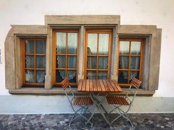 Empty chairs and table against window of building