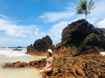 Young woman on rock at beach against sky