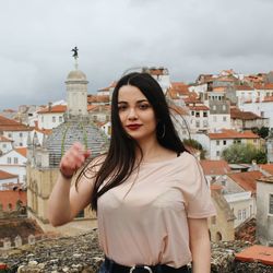 Portrait of young woman standing against buildings in city