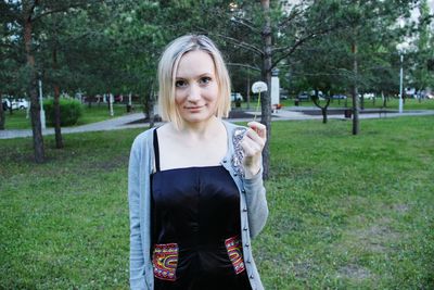 Portrait of young woman holding dandelion at park