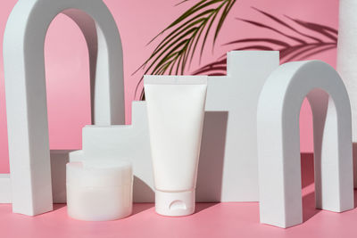 White blank cosmetic product bottles on pink background with palm branch, as advertisement. 