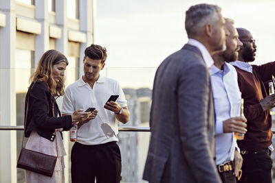 Professionals talking over smart phones while colleagues enjoying in office party after work