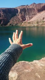 Close-up of hand reaching lake against mountains