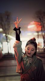 Smiling young woman gesturing peace sign while standing on road at night