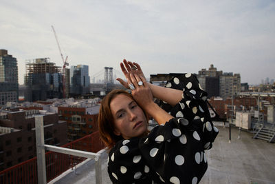 Portrait of young woman standing against buildings in city