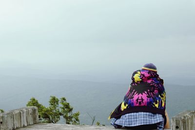 Rear view of woman sitting on observation point during foggy weather