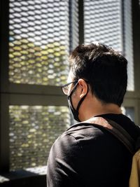 Rear view of young man wearing glasses against window.