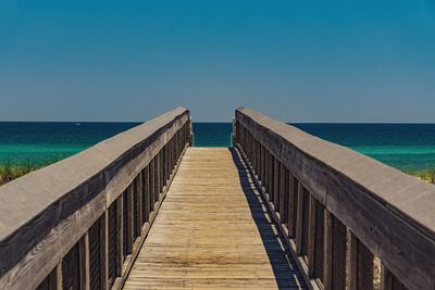 Pier over sea against clear blue sky