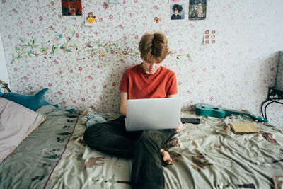 Rear view of woman using digital tablet while sitting on bed at home