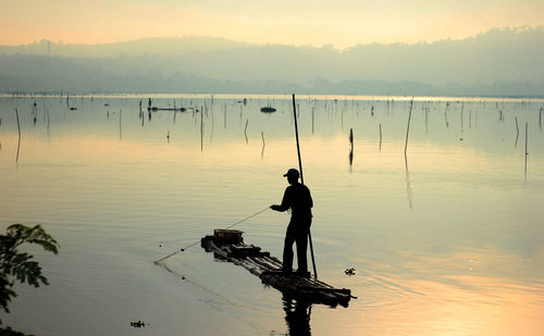 Silhouette man fishing in lake against sky during sunset