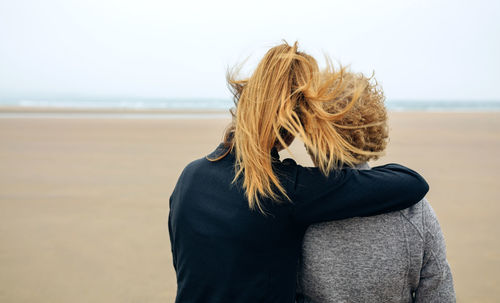 Rear view of woman with mother standing on beach against clear sky