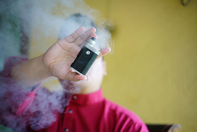 Man smoking electronic cigarette against yellow wall