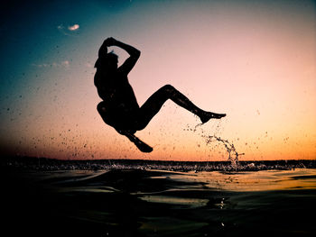 Silhouette man with arms raised against sky during sunset