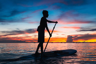 Silhouette man sailing boat in sea against sky during sunset