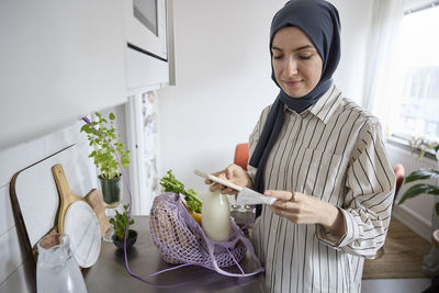 Woman in headscarf unpacking groceries at home and checking receipt