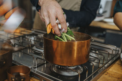 Chef putting vegetables in copper saucepan while making broth soup in kitchen