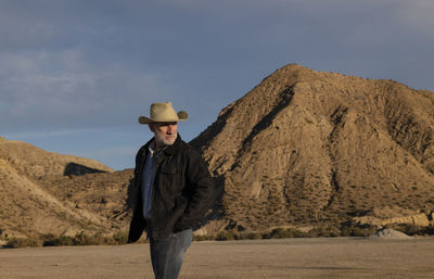 Adult man in cowboy hat standing against mountains in tabernas desert. almeria, spain