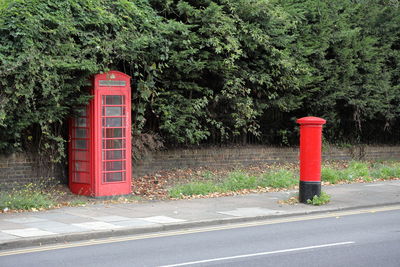 Red mailbox by road against trees and plants