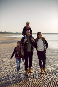 Family in a leather jacket walks along the beach with their dog in autumn