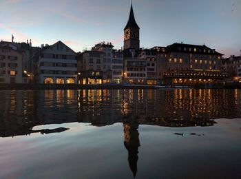 Buildings and lake against sky in city at dusk